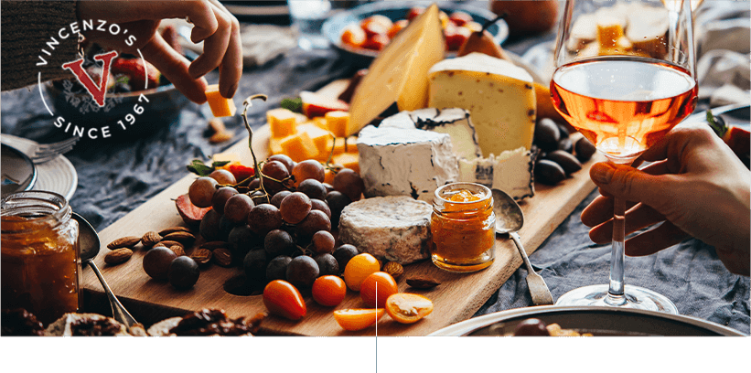 Charcuterie board filled with cheese and fruits, friends digging in and enjoying wine.